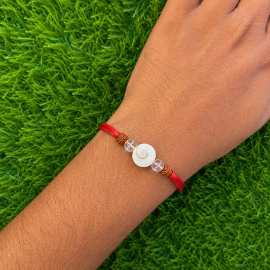 Bracelet with a red cord and white bead on a wrist against a green grass background